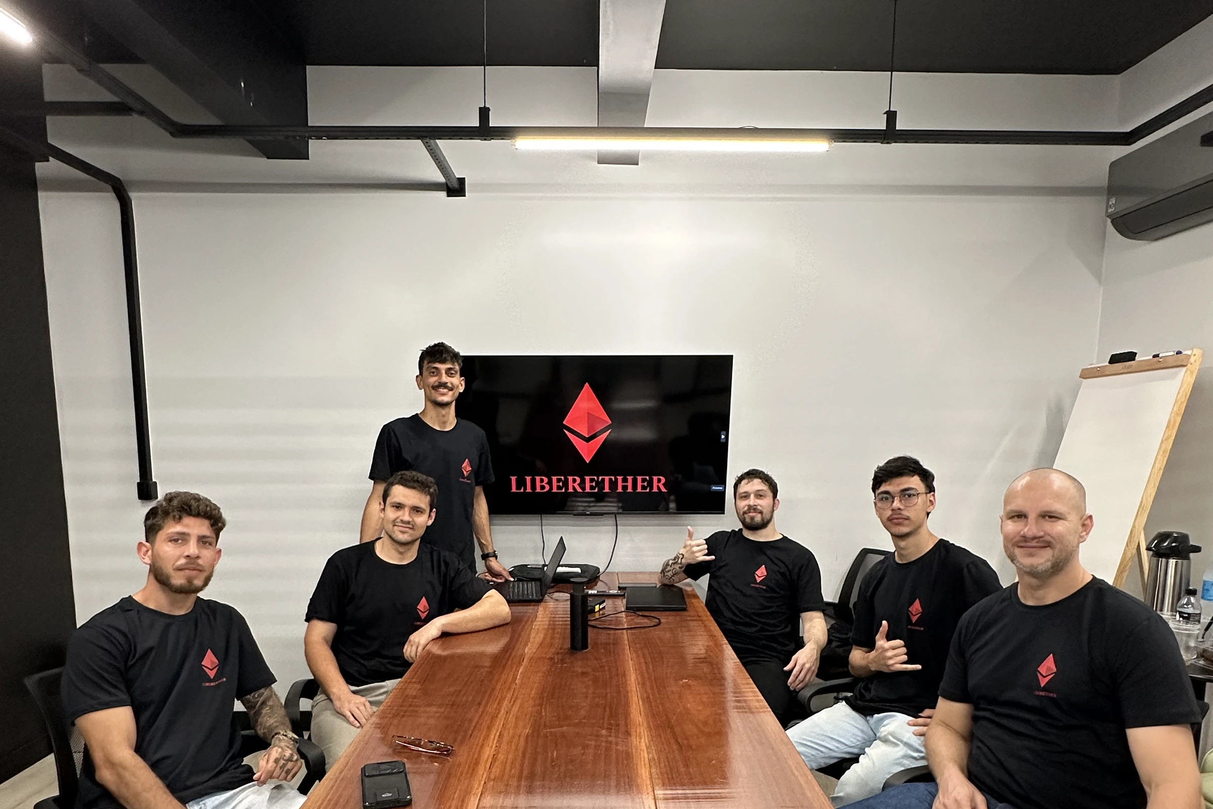 Time da LiberEther com camisetas da marca em volta da mesa de trabalho