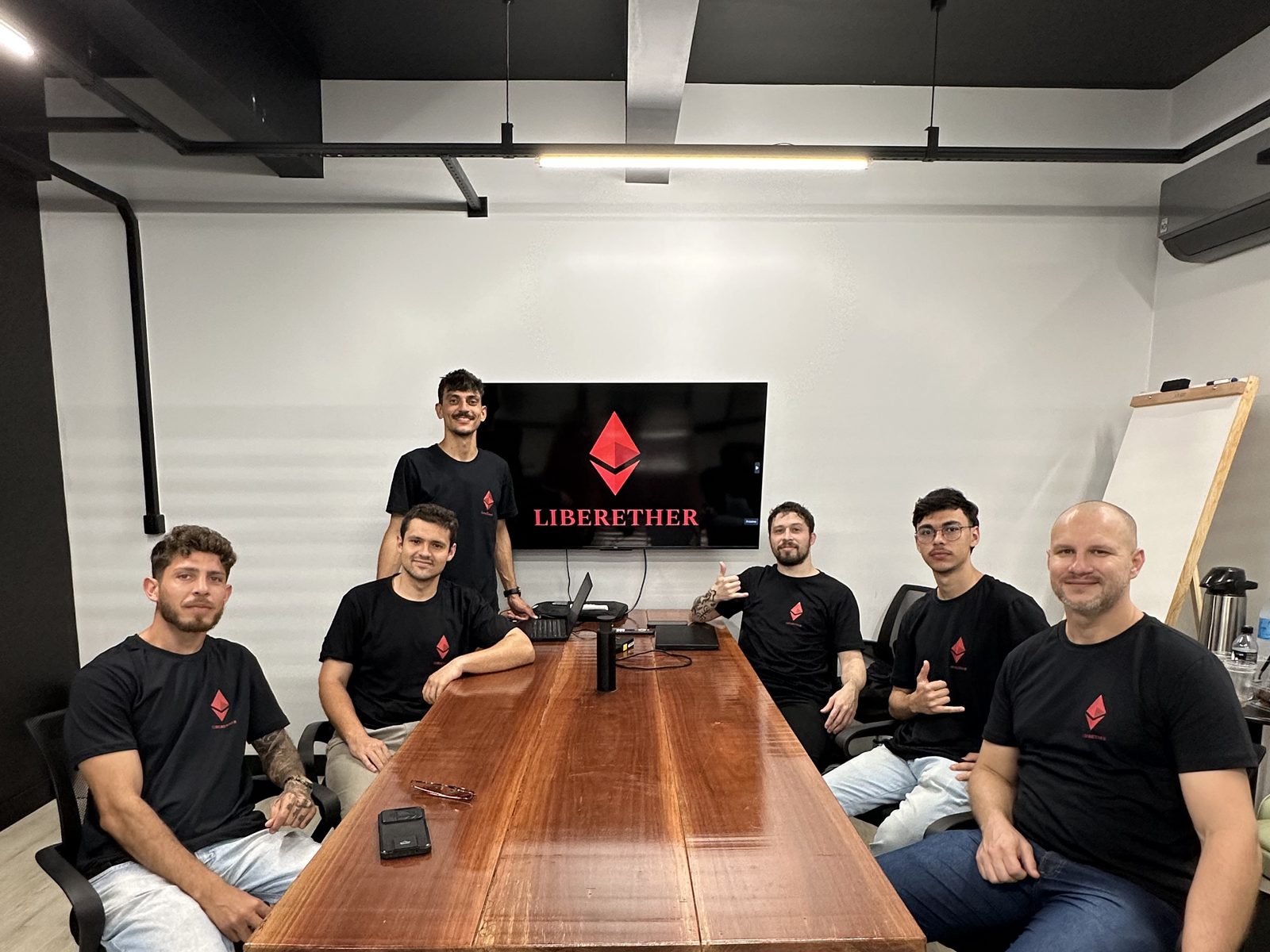Encuentro de la comunidad LiberEther alrededor de la mesa, con la marca en pantalla